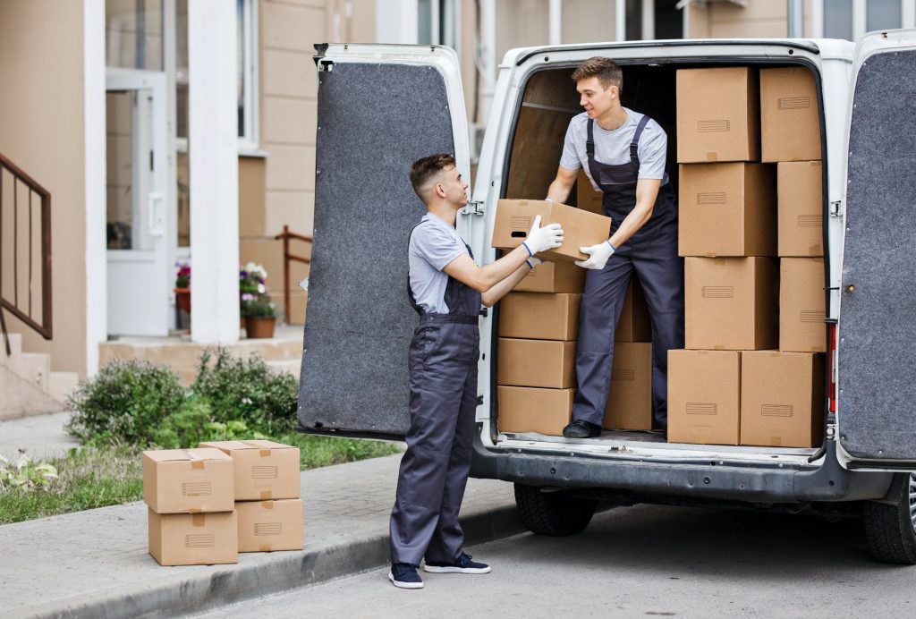 Two young handsome movers wearing uniforms are unloading the van full of boxes. House move, mover